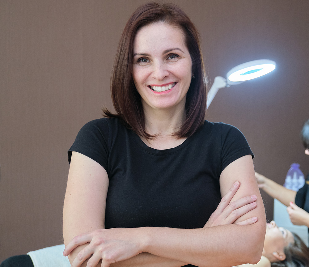 Portrait of manicurist holding tools in her hands wearing gloves and white clothes on white background.